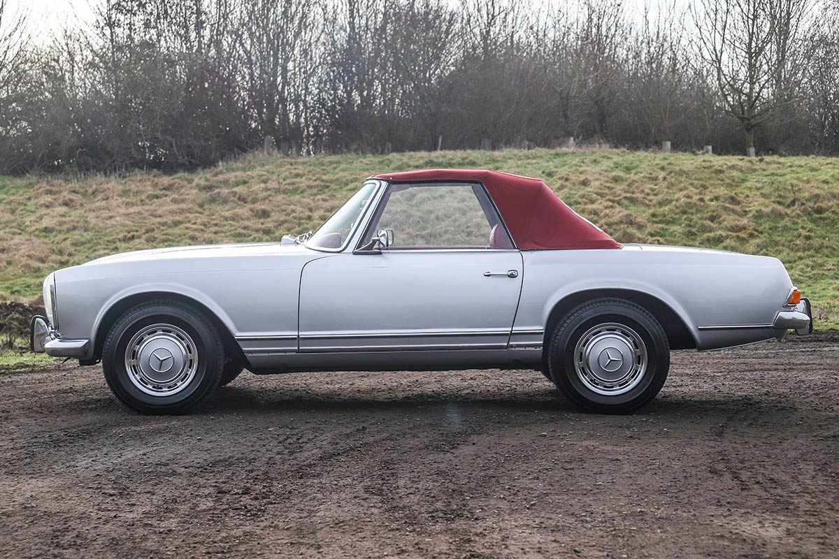 Side of a 280SL pagoda with a red soft top hood.